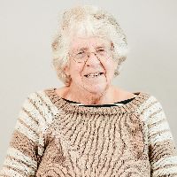 Mary Sanders has short white hair, wears glasses, and is wearing a light brown sweater