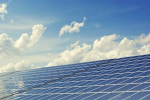 Solar panels in the foreground with a clear blue sky and fluffy white clouds in the background.