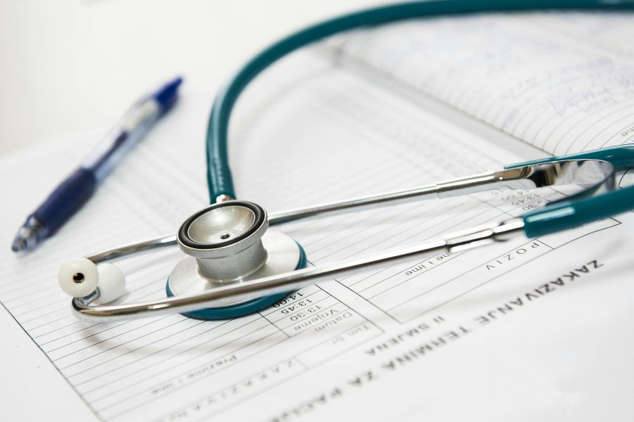 A doctor's stethoscope and a pen sitting on top of paperwork on a desk