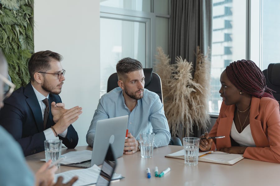 A group of people sitting round a table having a serious discussion. A laptop is open and notebooks and glasses of water are on the table