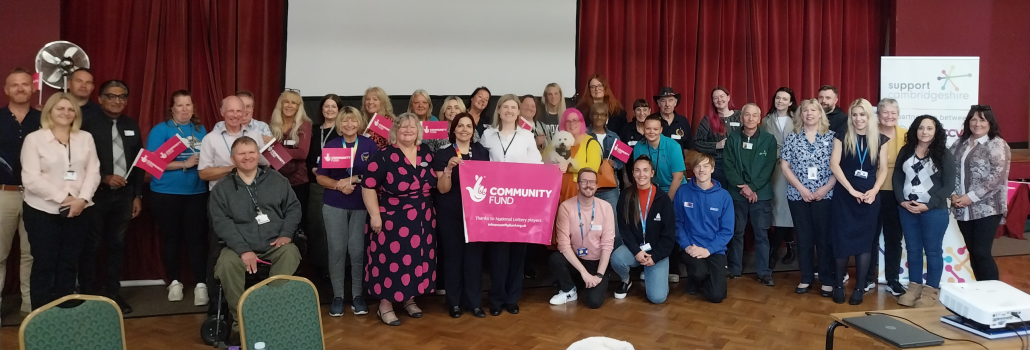 A diverse group of people stands together in a hall, smiling and holding a pink "Community Fund" banner, at the launch of the project 