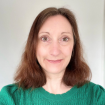 Karen has shoulder length brown hair and brown eyes. She is wearing a bright green jumper.