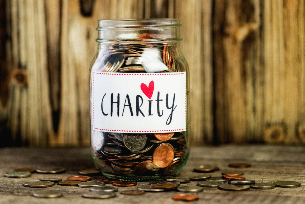 A jar full of coins with a white label with Charity in red text. A red heart hovers over the word