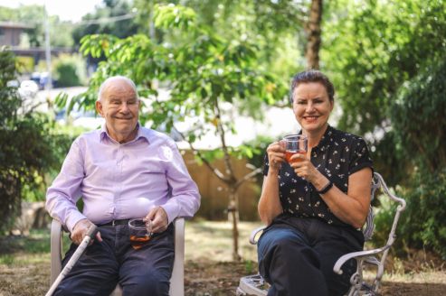 An older man and a woman sitting together in a garden drinking tea and smiling