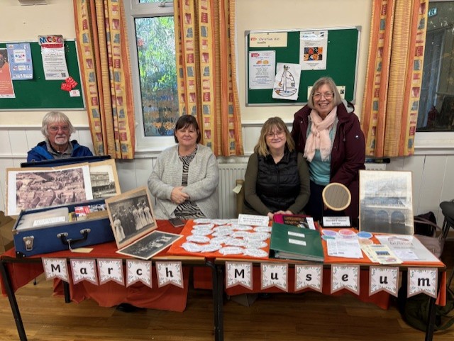 Four volunteer fair stallholders behind their stall. They are all smiling and look welcoming to visitors