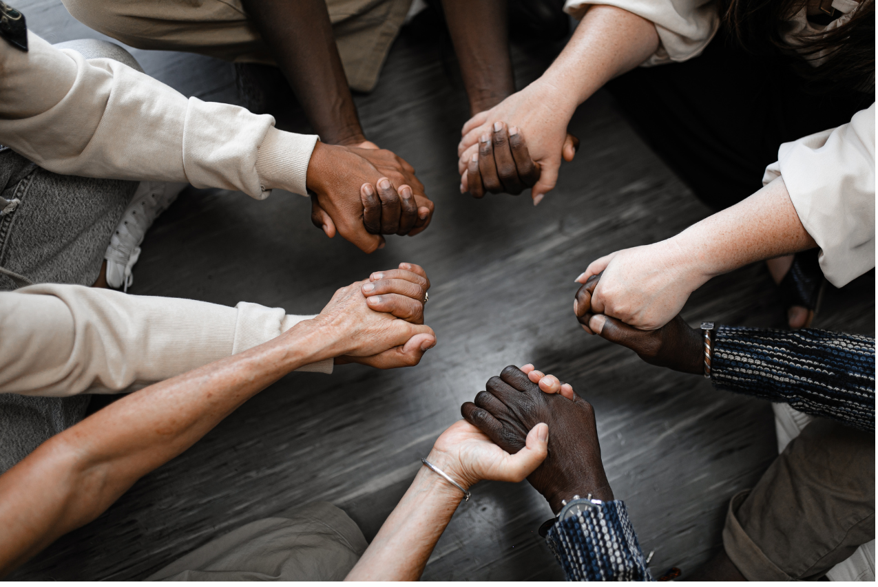 A circle of hands of black, brown and white hands holding each other